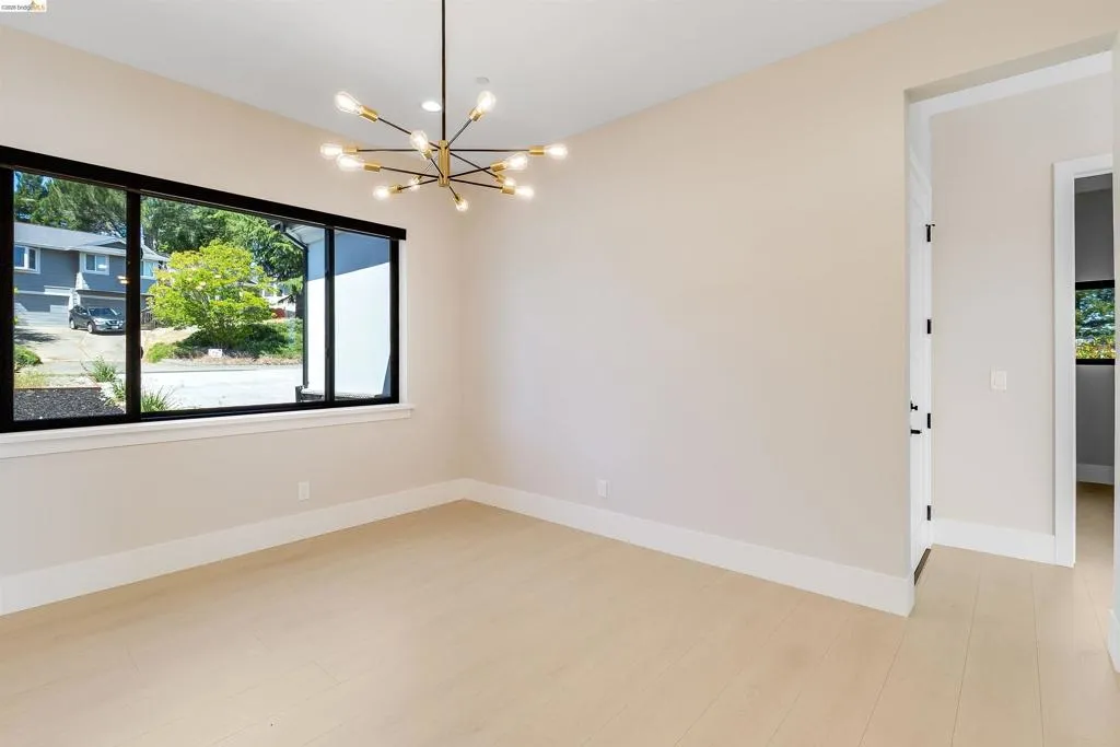 Spacious room featuring light wood-finish flooring, a contemporary sputnik chandelier, large windows with black framing, and a neutral wall palette