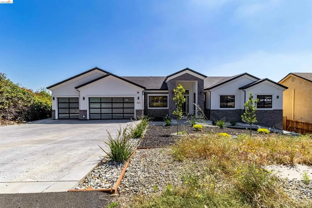 Contemporary architectural design featuring a white stucco and stacked stone exterior, multi-panel garage doors, a covered entry, and a landscaped front yard