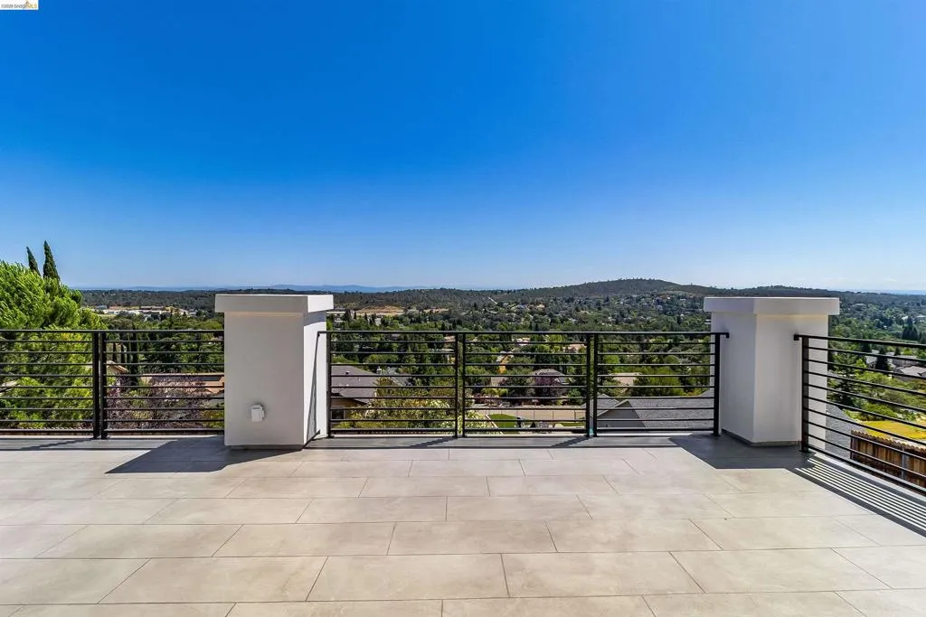 Expansive outdoor terrace featuring large format tile flooring, black horizontal bar railings, and white architectural columns