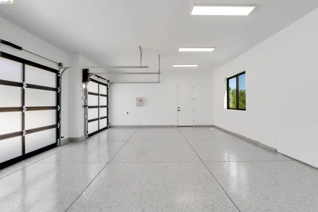 Spacious multi-bay garage featuring two frosted panel garage doors, an epoxy-coated concrete floor, bright overhead lighting, and a side window