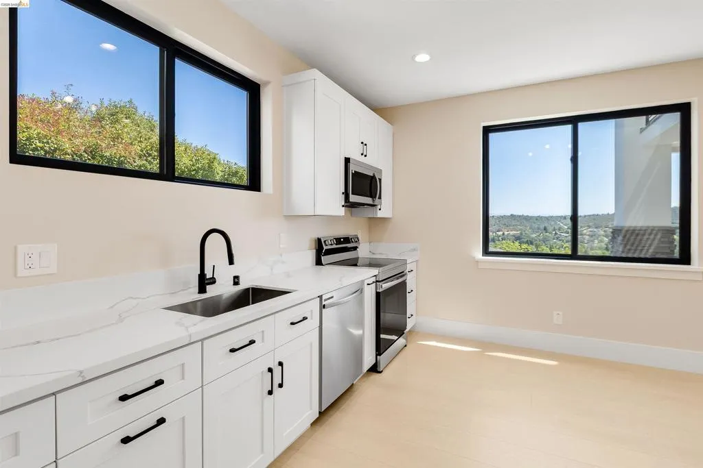 Modern kitchen featuring light wood-finish flooring, white cabinetry with matte black hardware, stone countertops, and stainless steel appliances