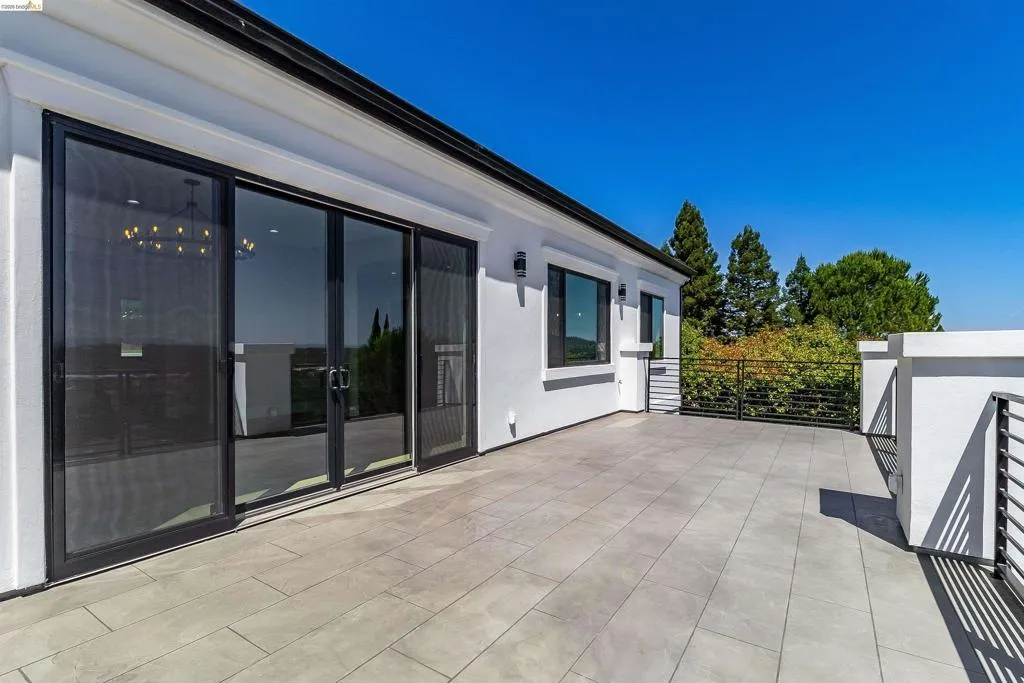 Spacious outdoor patio featuring light-toned tile flooring, contemporary black metal railings, and a crisp white stucco exterior
