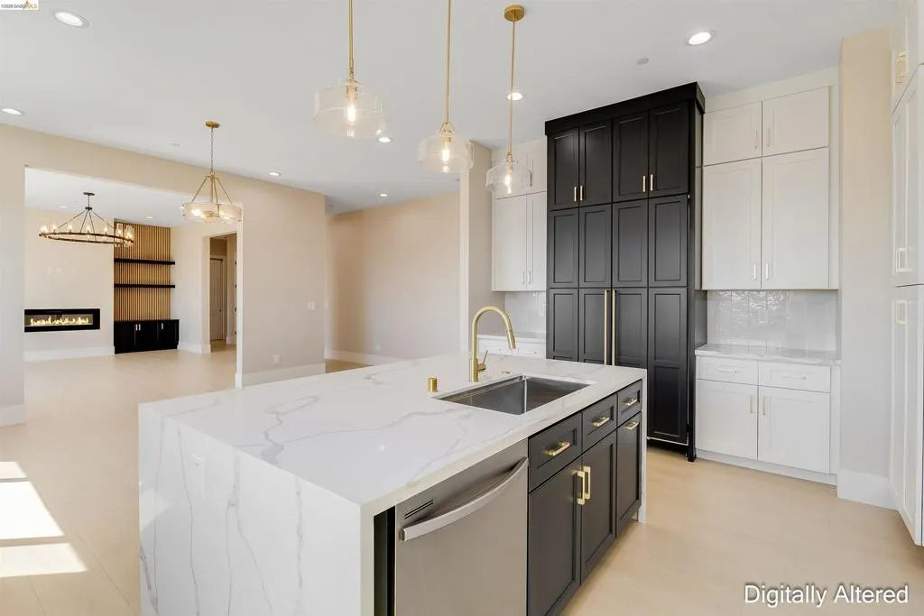 Spacious kitchen featuring a waterfall-edge island with an undermount sink, gold-tone faucet, and integrated dishwasher, alongside two-tone cabinetry with gold-tone hardware, and light wood-finish flooring