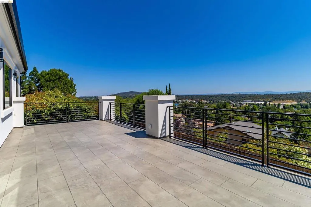 Expansive outdoor terrace featuring large format tile flooring, black horizontal bar railing, and plaster-finished pillars
