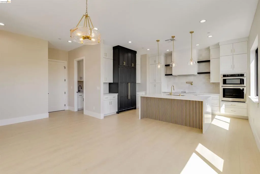 Open-concept kitchen featuring an island with slatted wood-finish paneling, white shaker cabinetry, stainless steel appliances, and wood-finish flooring