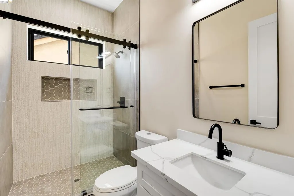 Contemporary bathroom featuring a frameless glass shower enclosure with matte black hardware, hexagon tile flooring, and a built-in shower niche