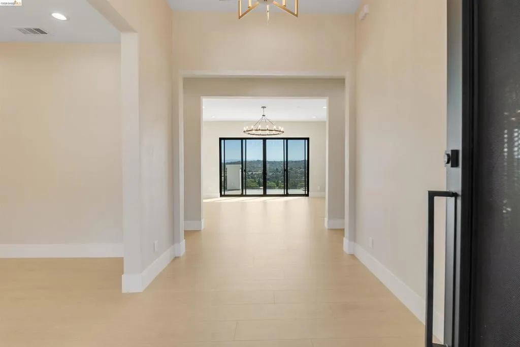 Light wood-finish flooring throughout, featuring a broad entryway leading to an open-concept interior with expansive folding glass doors