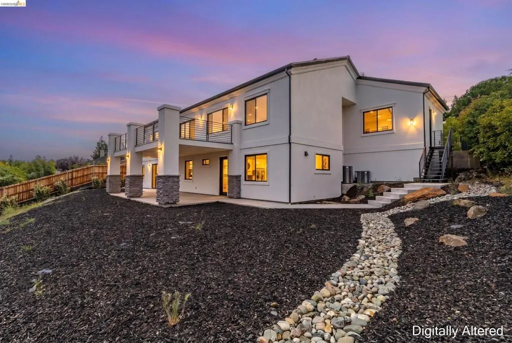 Contemporary stucco exterior featuring multiple balconies with metal railings, stone column accents, and a lower-level patio