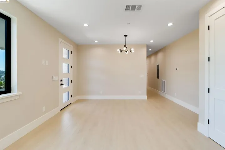 Spacious room with light wood-finish flooring, recessed lighting, and a contemporary chandelier