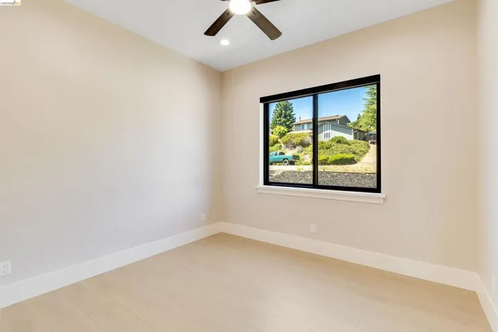 Bright room featuring wood-finish flooring, a large black-framed window, a ceiling fan, recessed lighting, and white baseboards