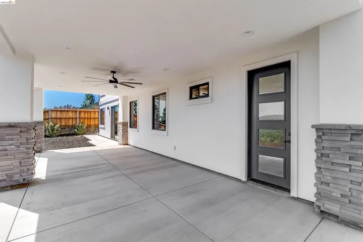 Covered patio featuring a concrete slab, stone veneer pillars, and a ceiling fan