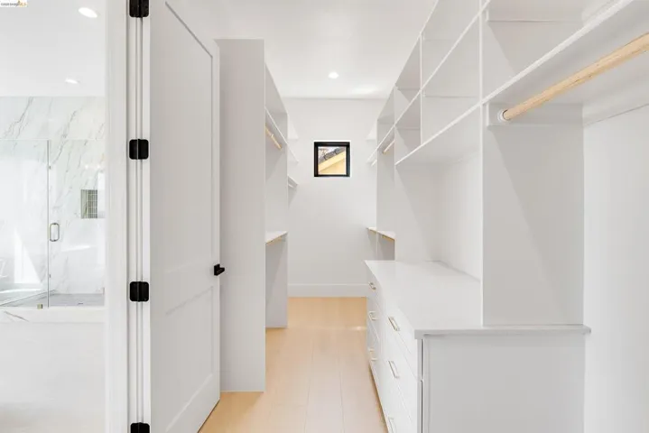 Spacious custom closet featuring extensive built-in shelving, integrated drawers with gold-tone hardware, wood-finish flooring, and a window