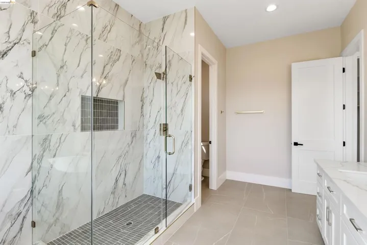 Glass-enclosed shower with large format marble-look tile walls and a mosaic tile floor