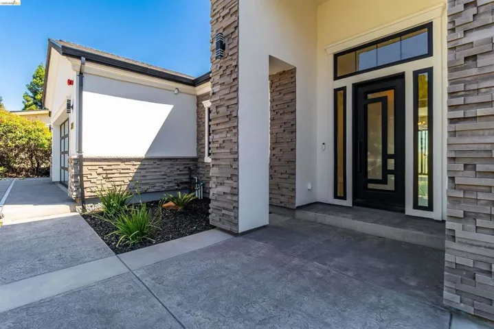 Contemporary entry featuring a black door with sidelights, transom window, and stone veneer accents