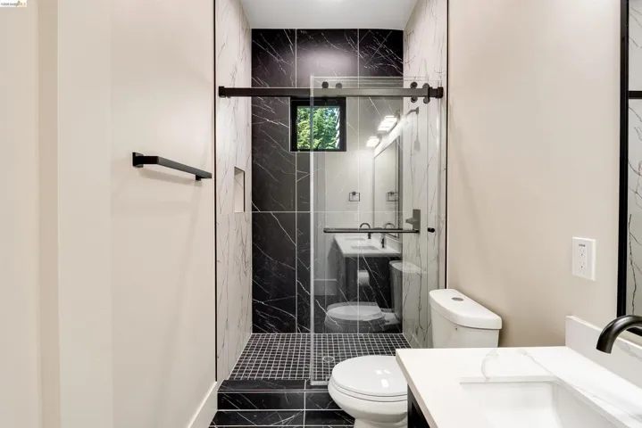 Contemporary bathroom featuring a glass-enclosed shower with a sliding door, black marble-look wall tiling, and square mosaic floor tiling