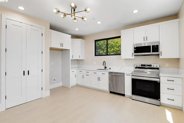 Modern kitchen featuring white shaker cabinetry, stainless steel appliances, light wood-finish flooring, recessed lighting, and a contemporary chandelier