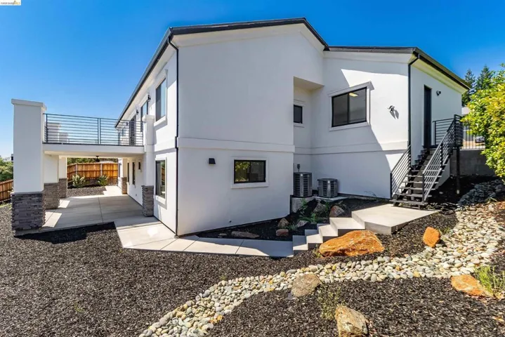 Contemporary white stucco exterior with black trim windows, a metal railing balcony, and a covered patio area