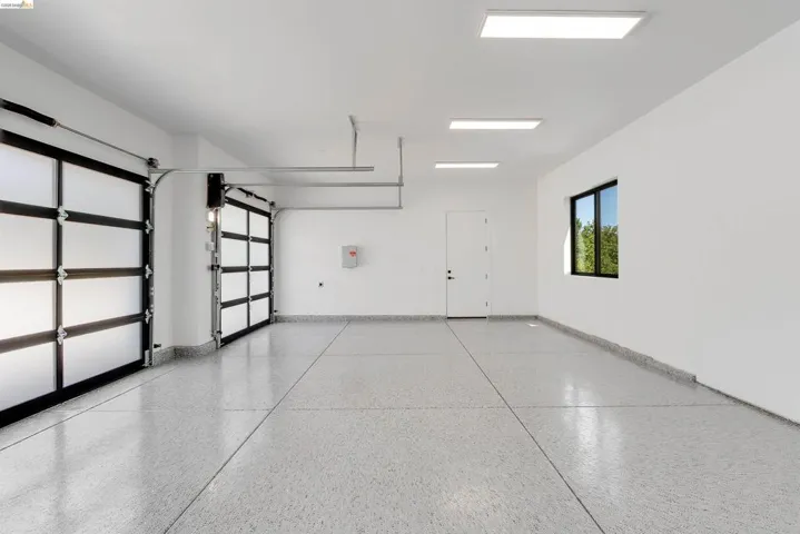 Spacious multi-bay garage featuring two frosted panel garage doors, an epoxy-coated concrete floor, bright overhead lighting, and a side window