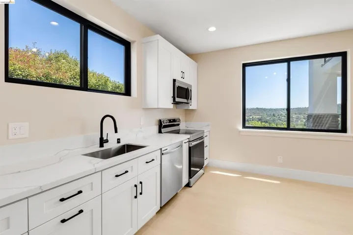Modern kitchen featuring light wood-finish flooring, white cabinetry with matte black hardware, stone countertops, and stainless steel appliances