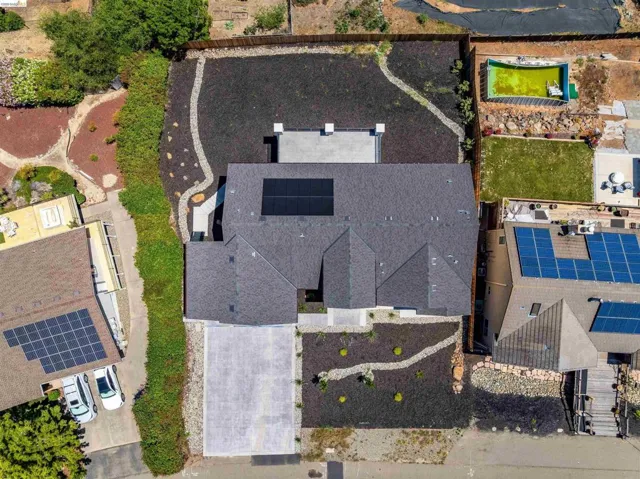 Contemporary residence featuring a dark shingle roof, solar panel installation, and a spacious paved driveway