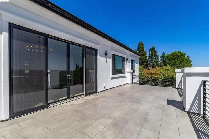 Spacious outdoor patio featuring light-toned tile flooring, contemporary black metal railings, and a crisp white stucco exterior