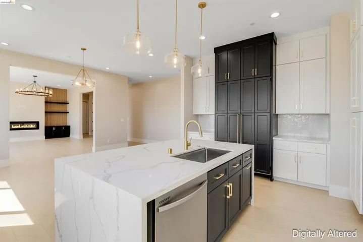 Spacious kitchen featuring a waterfall-edge island with an undermount sink, gold-tone faucet, and integrated dishwasher, alongside two-tone cabinetry with gold-tone hardware, and light wood-finish flooring