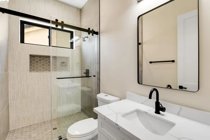 Contemporary bathroom featuring a frameless glass shower enclosure with matte black hardware, hexagon tile flooring, and a built-in shower niche