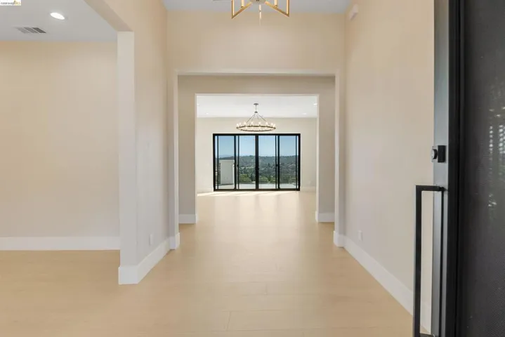Light wood-finish flooring throughout, featuring a broad entryway leading to an open-concept interior with expansive folding glass doors