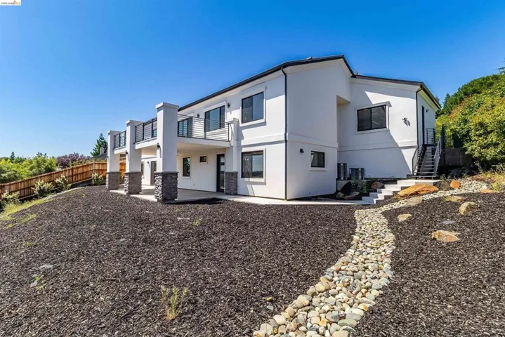 Multi-level contemporary stucco exterior with multiple balconies featuring black railings and stone-clad pillars