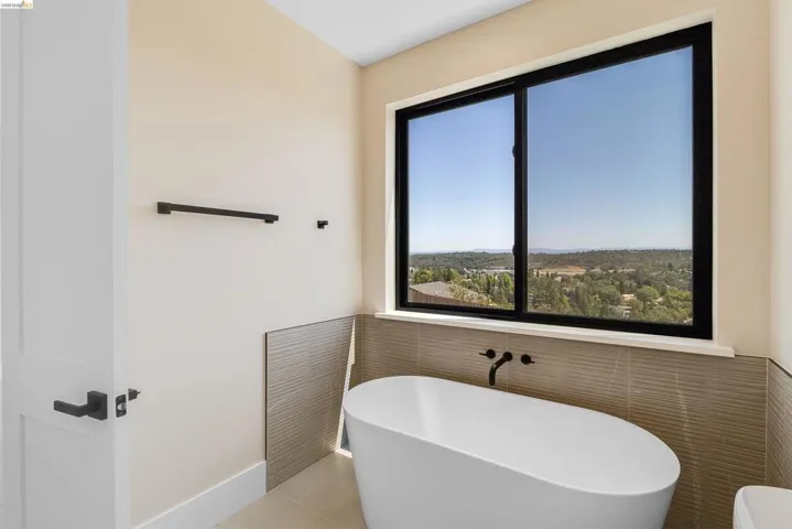 Freestanding soaking tub with a wall-mounted matte black faucet, set against a large window with black trim