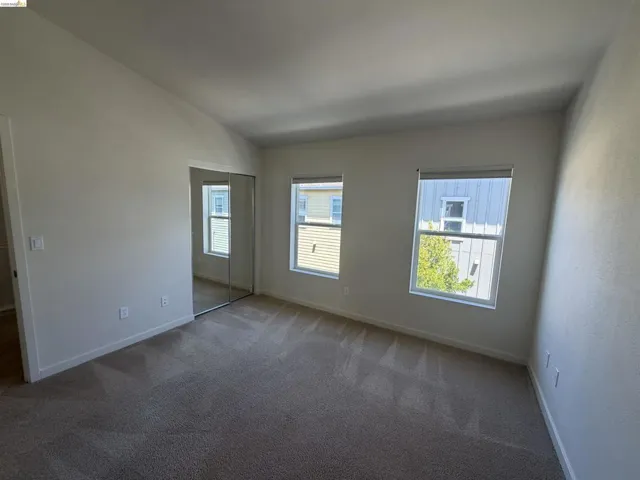 Carpeted room featuring two windows with roller shades, mirrored closet doors, and recessed lighting