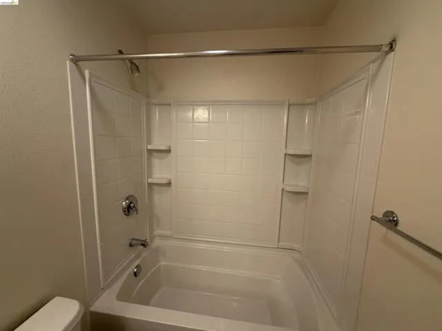 Bathtub with integrated shower surround, featuring a chrome showerhead and faucet