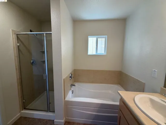 Bathroom featuring a glass-enclosed shower with integrated shelving, a built-in bathtub with a tiled surround, a vanity with an integrated sink, and a framed mirror
