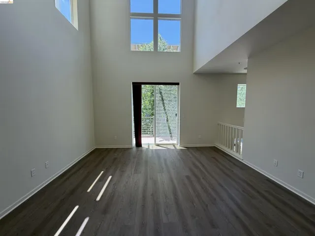 Spacious interior featuring high ceilings, wood-finish flooring, a sliding glass door to an outdoor balcony with metal railings, a white painted banister, and multiple upper-level windows