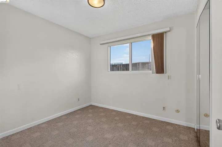 Bright room featuring a window with vertical blinds, textured white walls, and patterned carpet