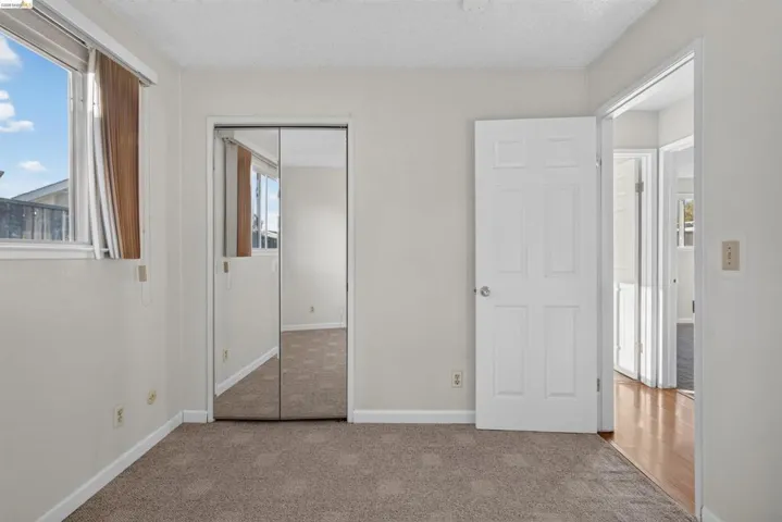 Carpeted room featuring a double-pane window, mirrored closet doors, a white paneled door, and neutral wall tones