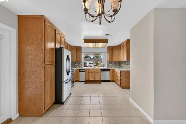 Kitchen featuring extensive wood cabinetry, tile flooring, stainless steel appliances, a mosaic tile backsplash, and a recessed window