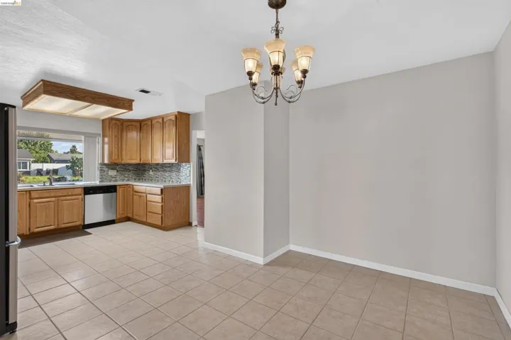 Kitchen and dining area featuring tile flooring, oak cabinetry, a white dishwasher, stainless steel refrigerator, and a decorative chandelier