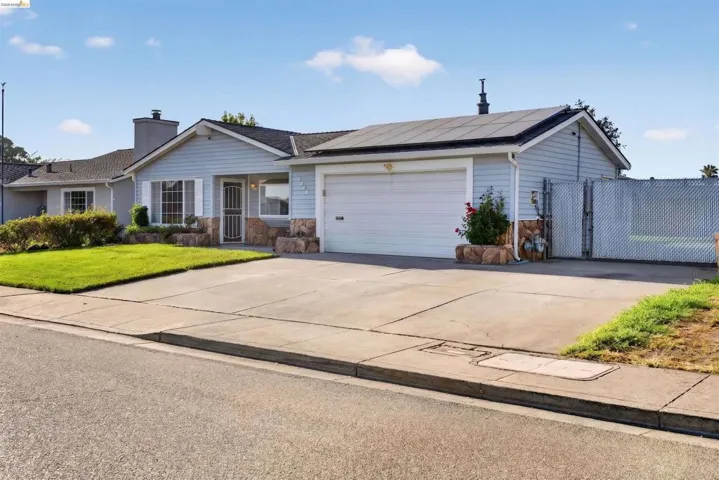 Single-story residence featuring light blue siding with stone accents, a two-car garage, and a chain-link fence