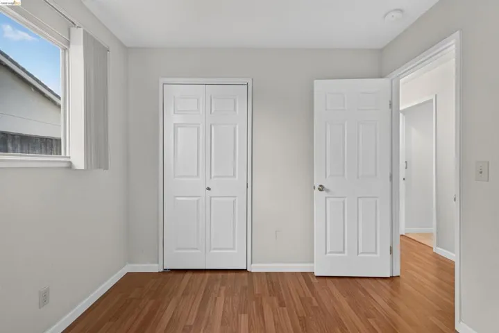 Room featuring wood-finish flooring, light gray walls, a window with vertical blinds, a six-panel door, and a bi-fold closet door
