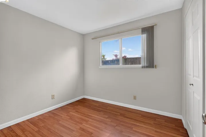 Bright interior space featuring wood-finish flooring, light grey painted walls, white baseboards, and a double-paned window