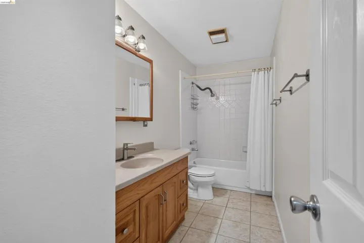 Bathroom featuring a wood-finish vanity with an integrated sink, a full-size tub with shower, tiled flooring, and a large wall mirror
