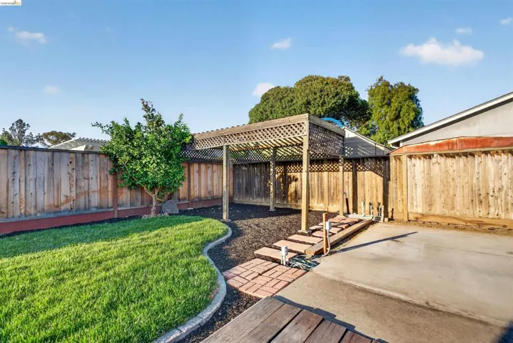 Backyard featuring a wooden pergola, brick pathway, and a grassy area with a curvilinear border