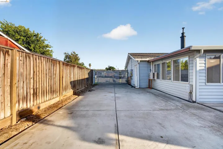 Expansive concrete driveway bordered by a tall wooden fence, offering ample exterior space