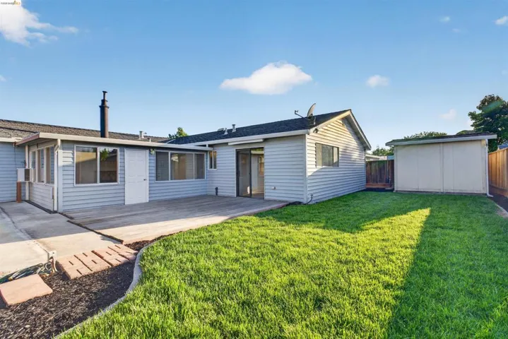 Spacious backyard featuring a large green lawn, concrete patio, and a storage shed