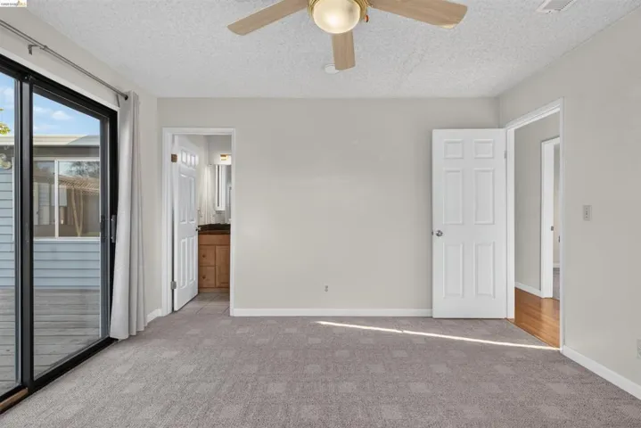 Spacious room with sliding glass door access to an outdoor deck, neutral-toned carpeting, ceiling fan with light fixture, and a white six-panel interior door