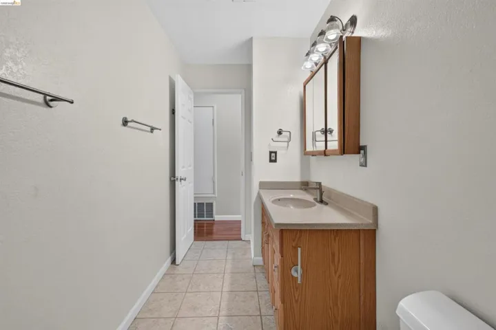 Bathroom featuring a wood-finish vanity with an integrated sink and light-toned countertop, tile flooring, and a mirrored medicine cabinet with overhead lighting