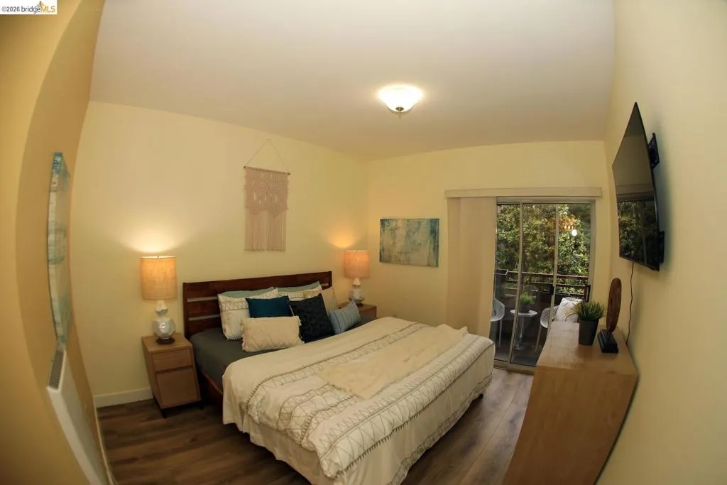Bedroom featuring wood-finish flooring, a ceiling-mounted light fixture, and a sliding glass door providing access to an exterior balcony