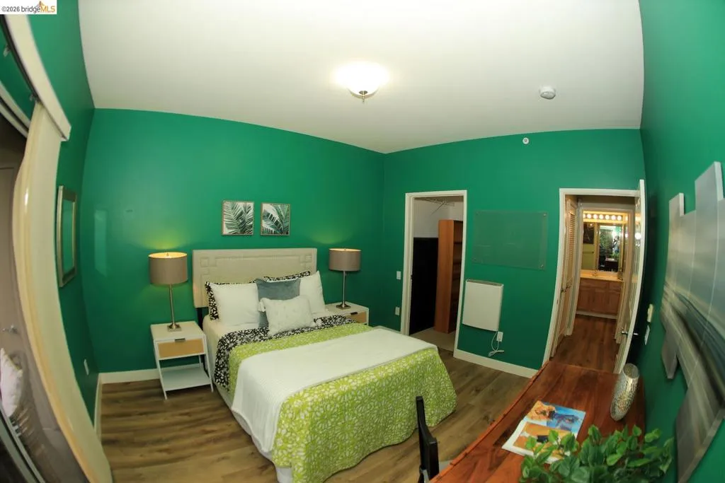 Bedroom featuring wood-finish flooring, a neutral upholstered headboard, and a built-in wall heater