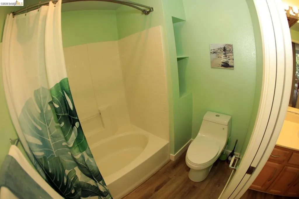 Bathroom featuring a full tub/shower combination with white surround, built-in shelving, wood-finish flooring, and a modern toilet